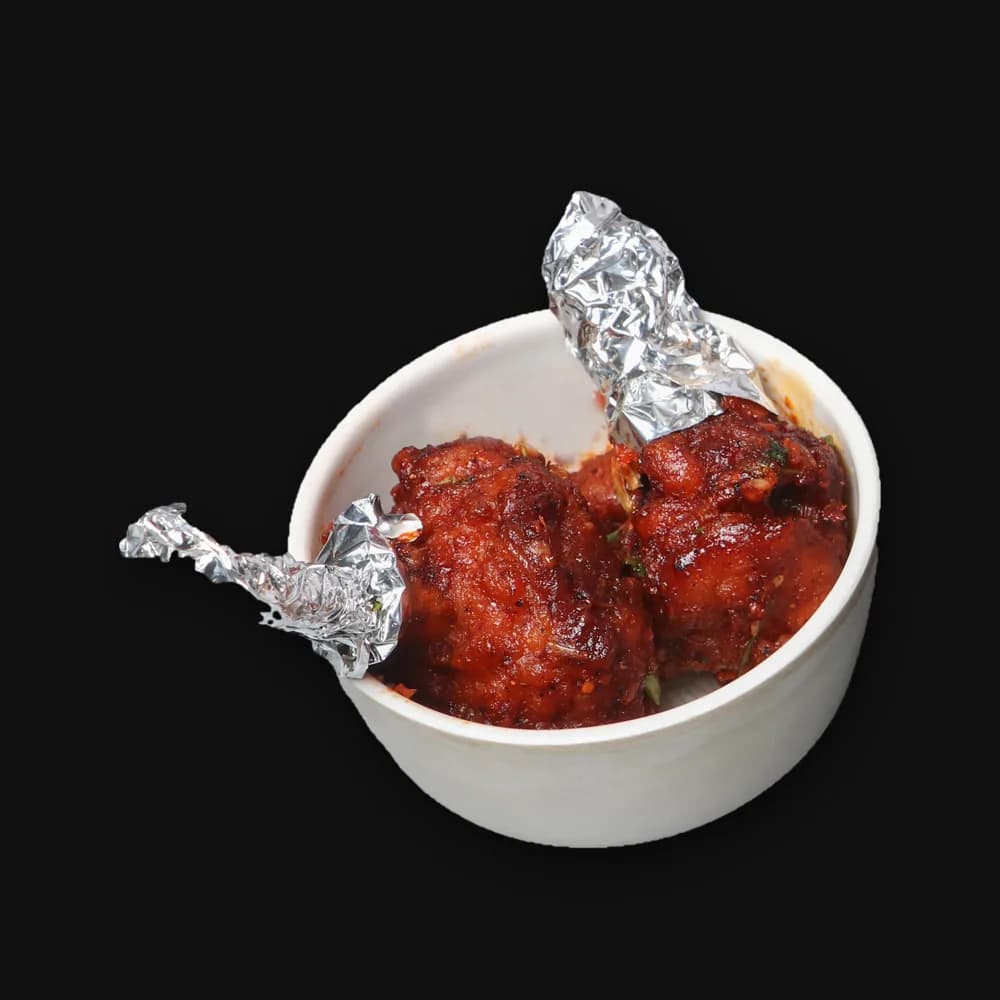 Two chicken lollipops in a small bowl