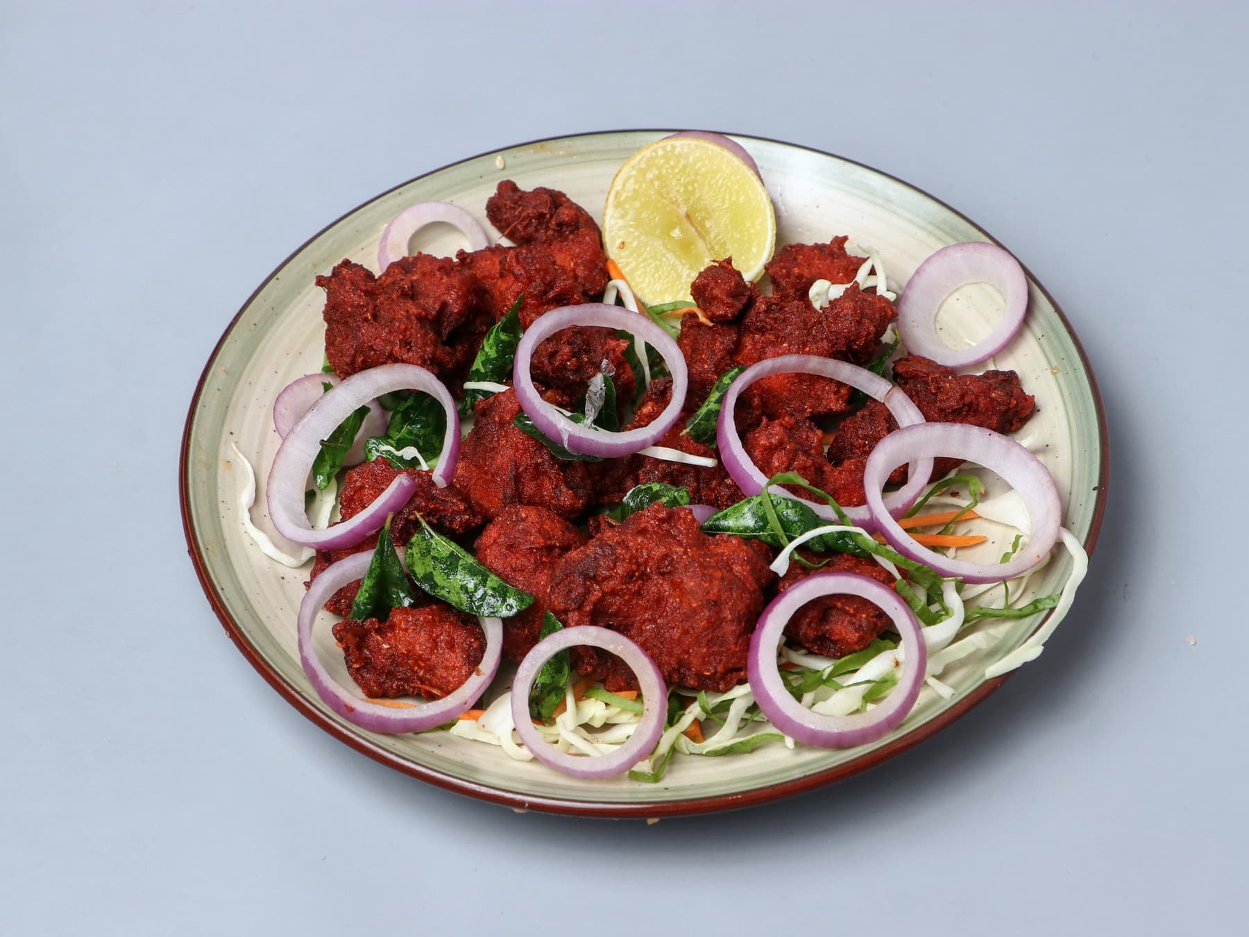 Crisp red Chicken 65 with onion rings, curry leaves and lemon