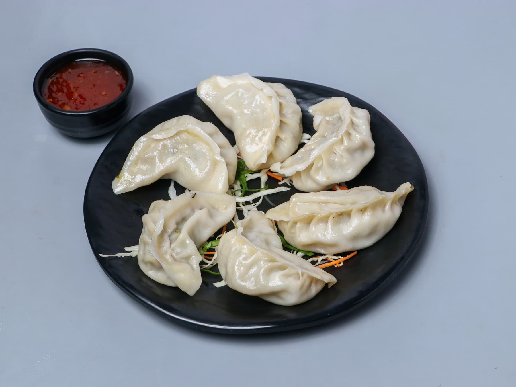 Steamed chicken momos with a chilli dip on a black plate