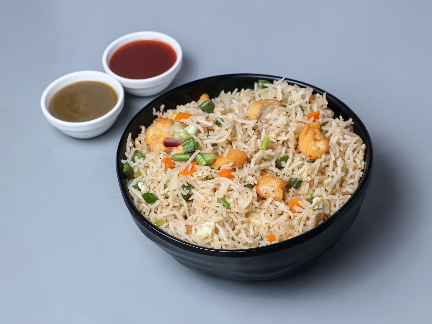 Chicken fried rice in a black bowl with two dips