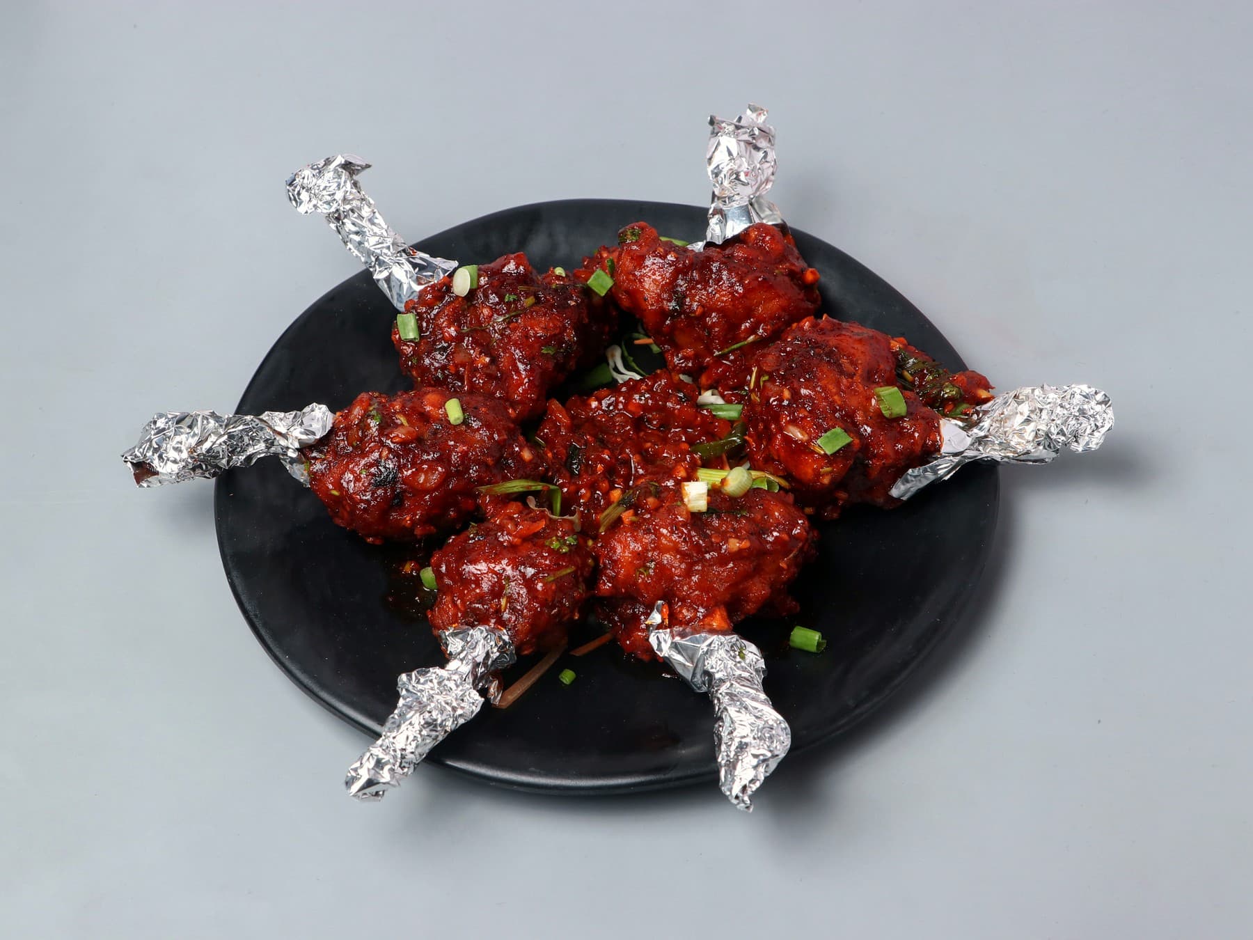 Chicken lollipops in a sticky red glaze on a black plate