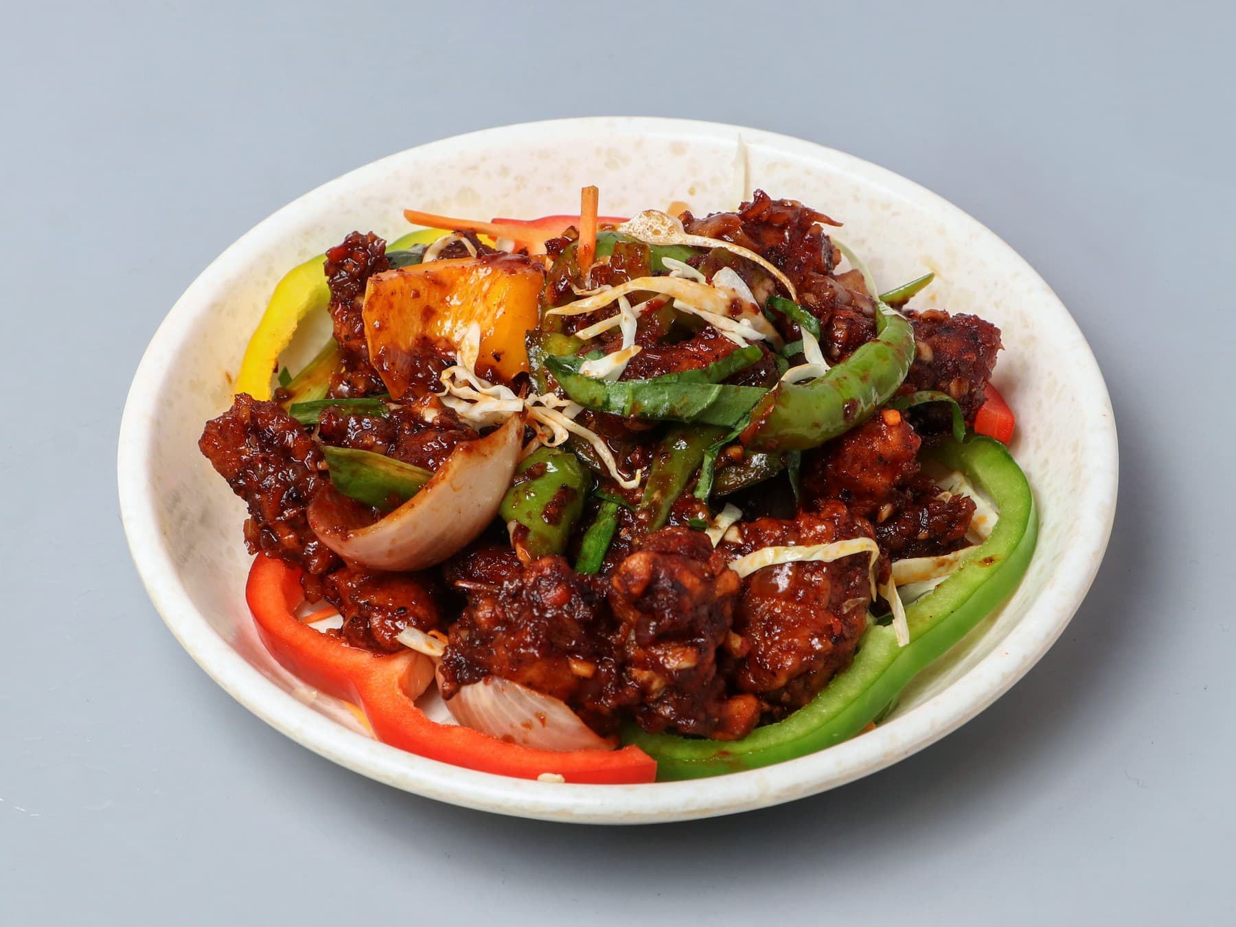 Chilli chicken tossed with peppers and onion on a speckled plate