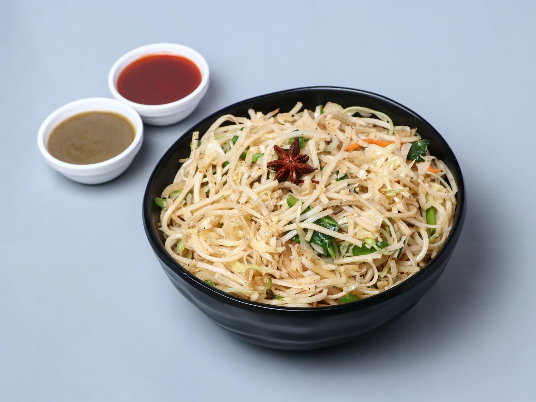 Hakka noodles with star anise in a black bowl with two dips