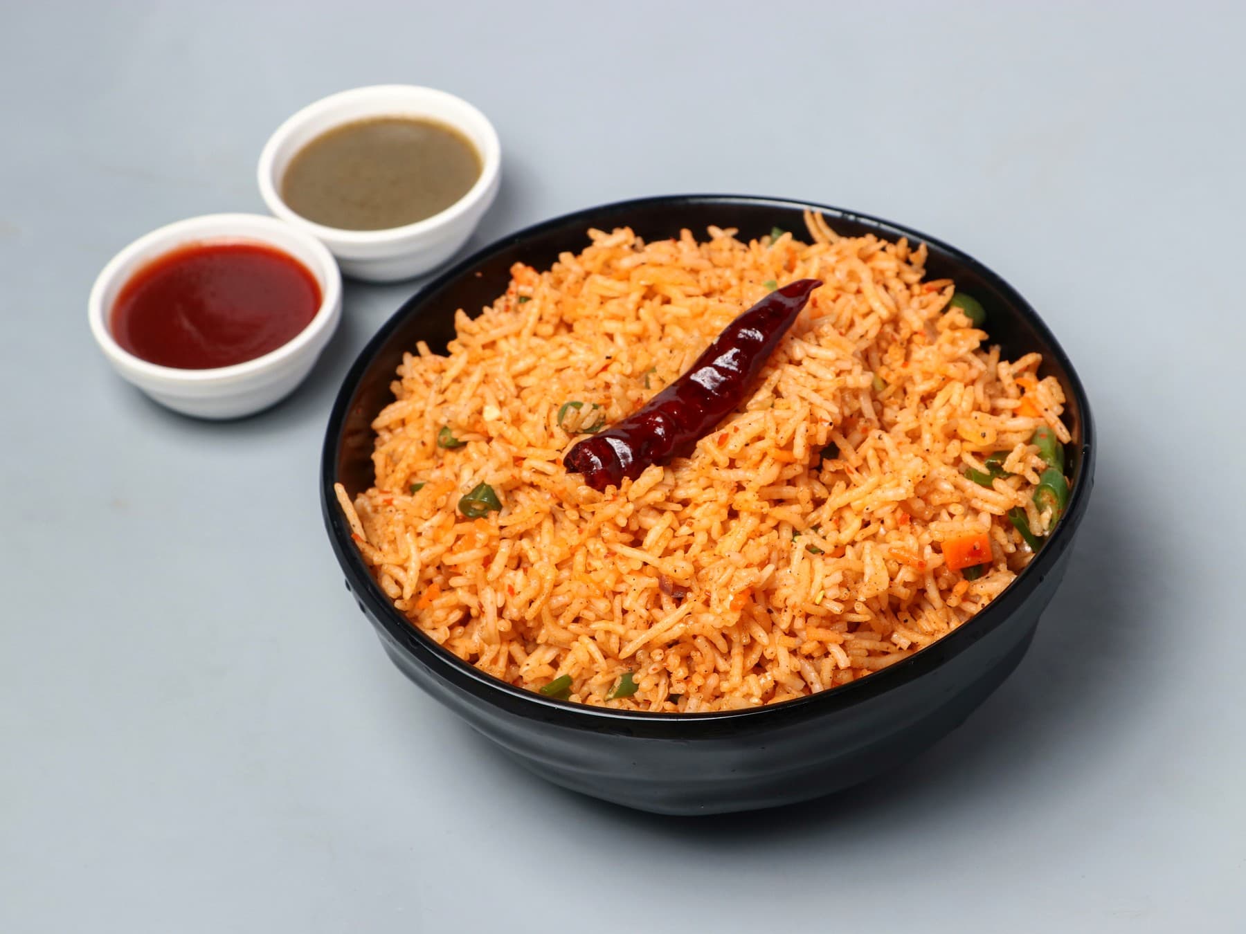 Red Schezwan fried rice with a dried chilli in a black bowl