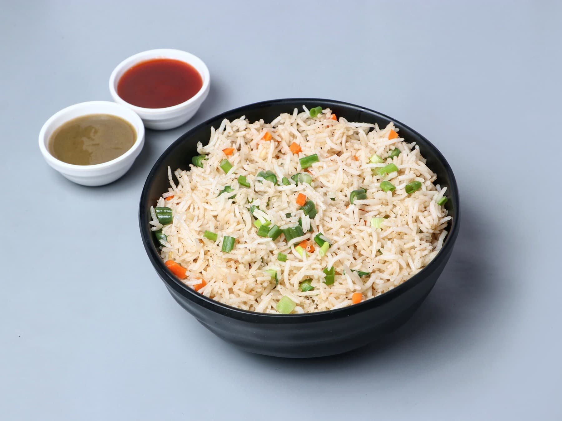 Vegetable fried rice in a black bowl with two dips