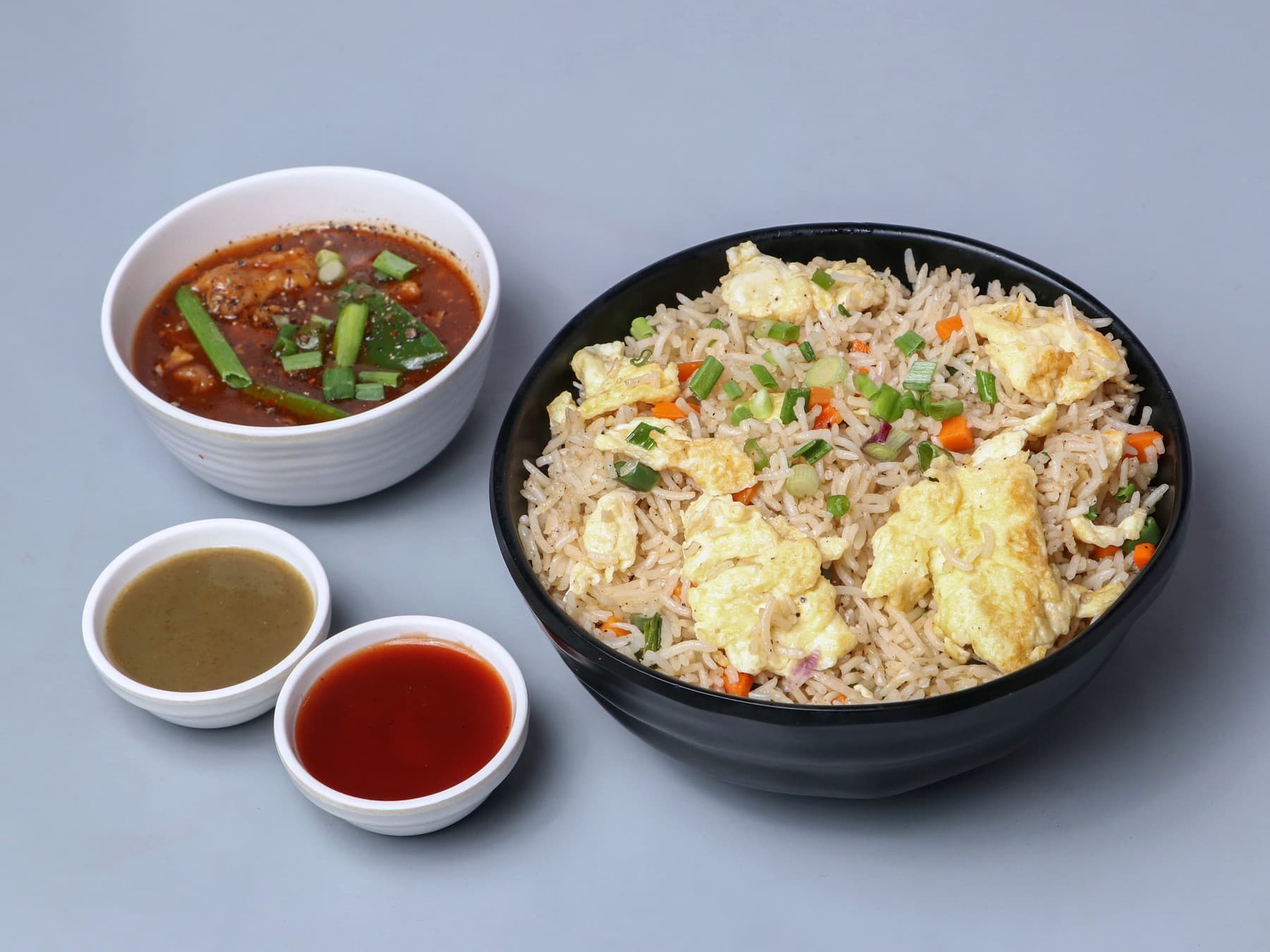 Egg fried rice in a black bowl with a side of pepper chicken gravy