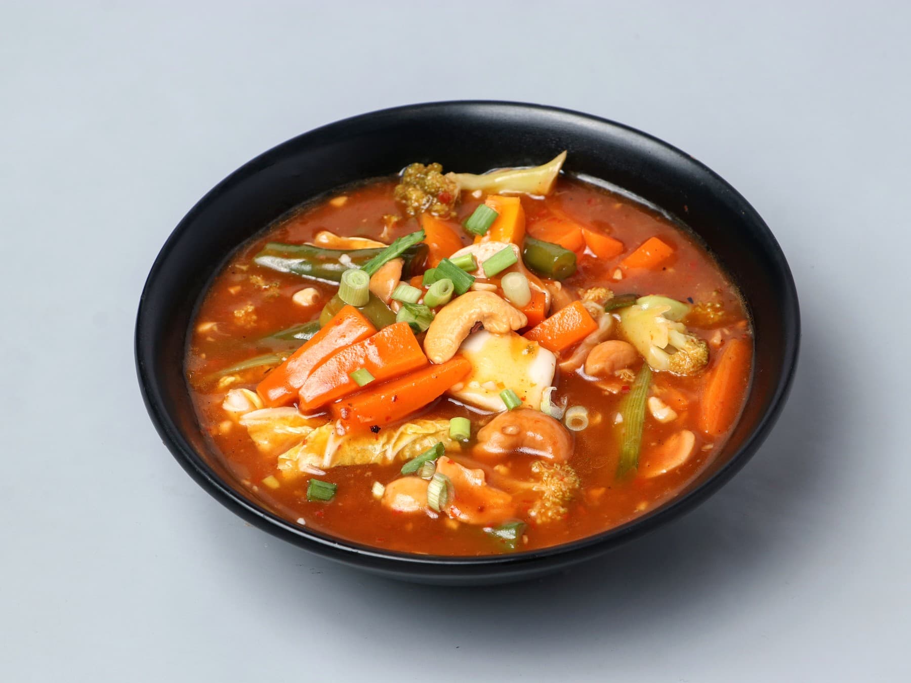 Mixed vegetables and cashew nuts in a light red gravy in a black bowl