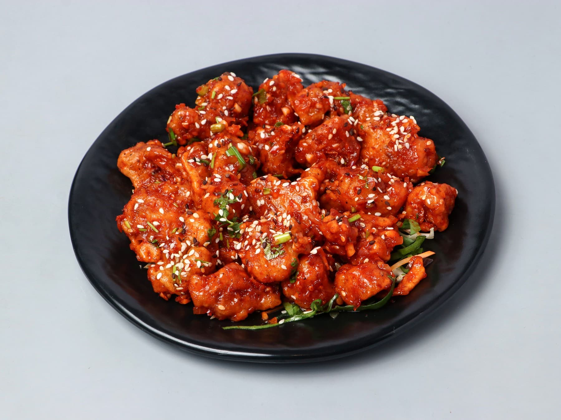 Cauliflower in a fiery red chilli glaze with sesame on a black plate